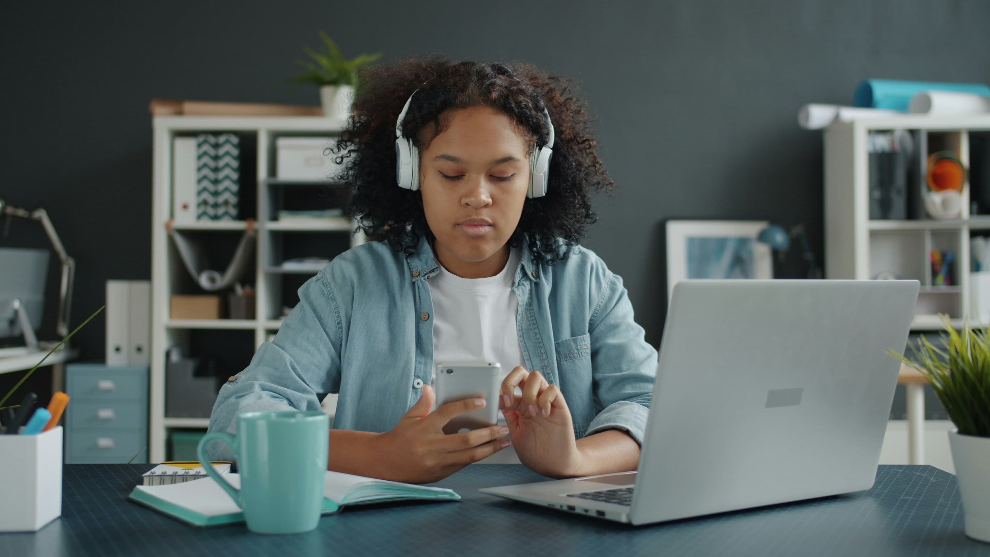 Young girl with headphones uses phone at desk