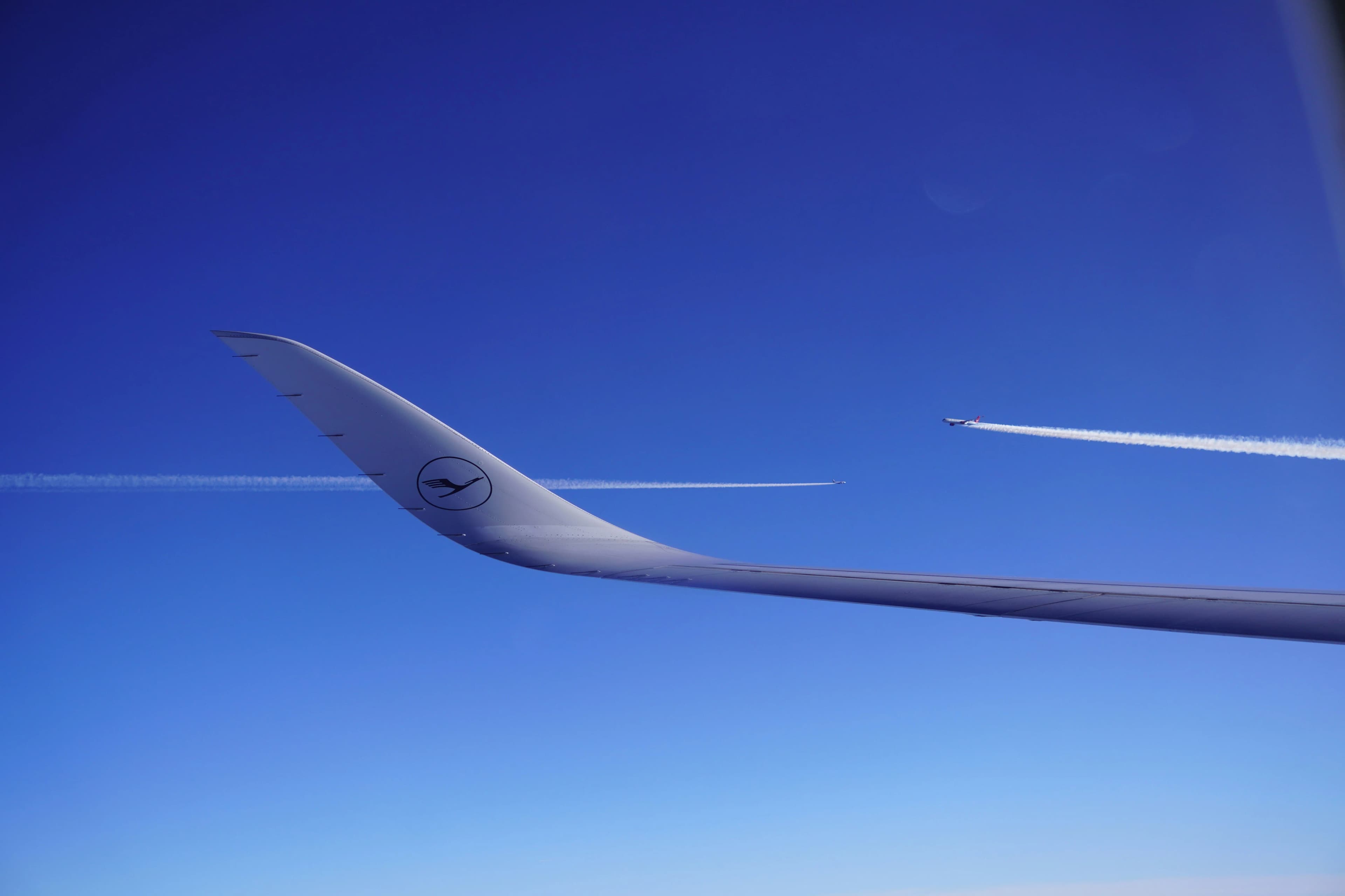 Plane wing against a bright blue sky with jet trails.