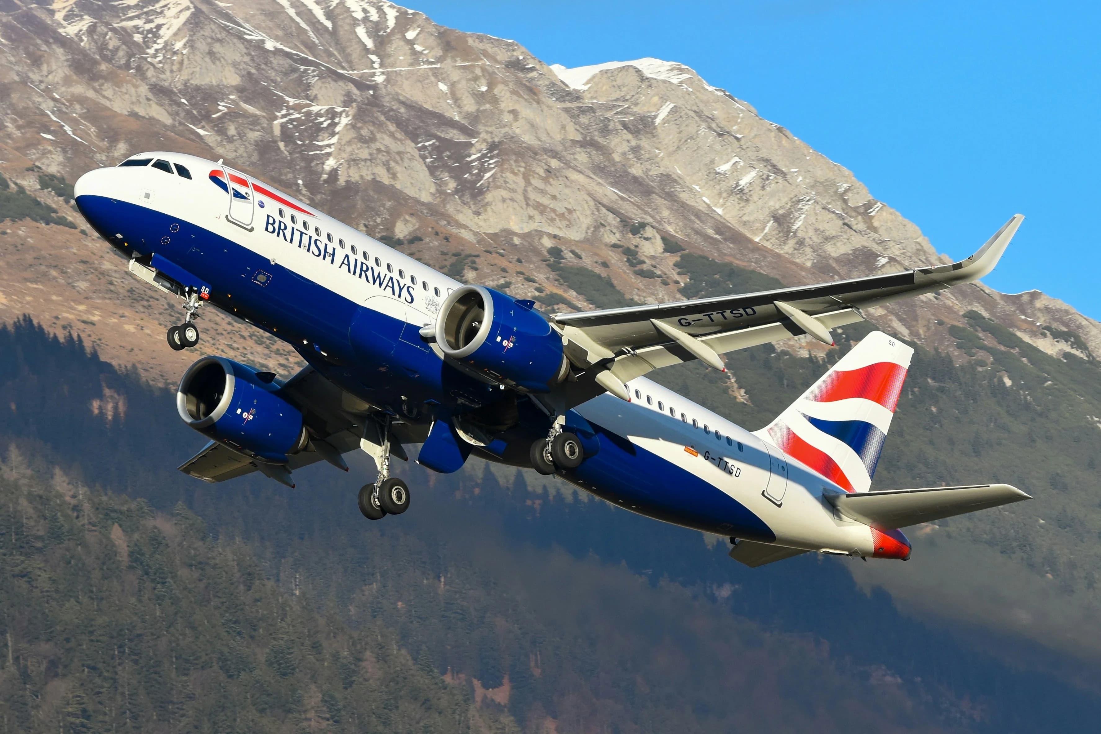 A british airways airplane ascending with mountains behind it.