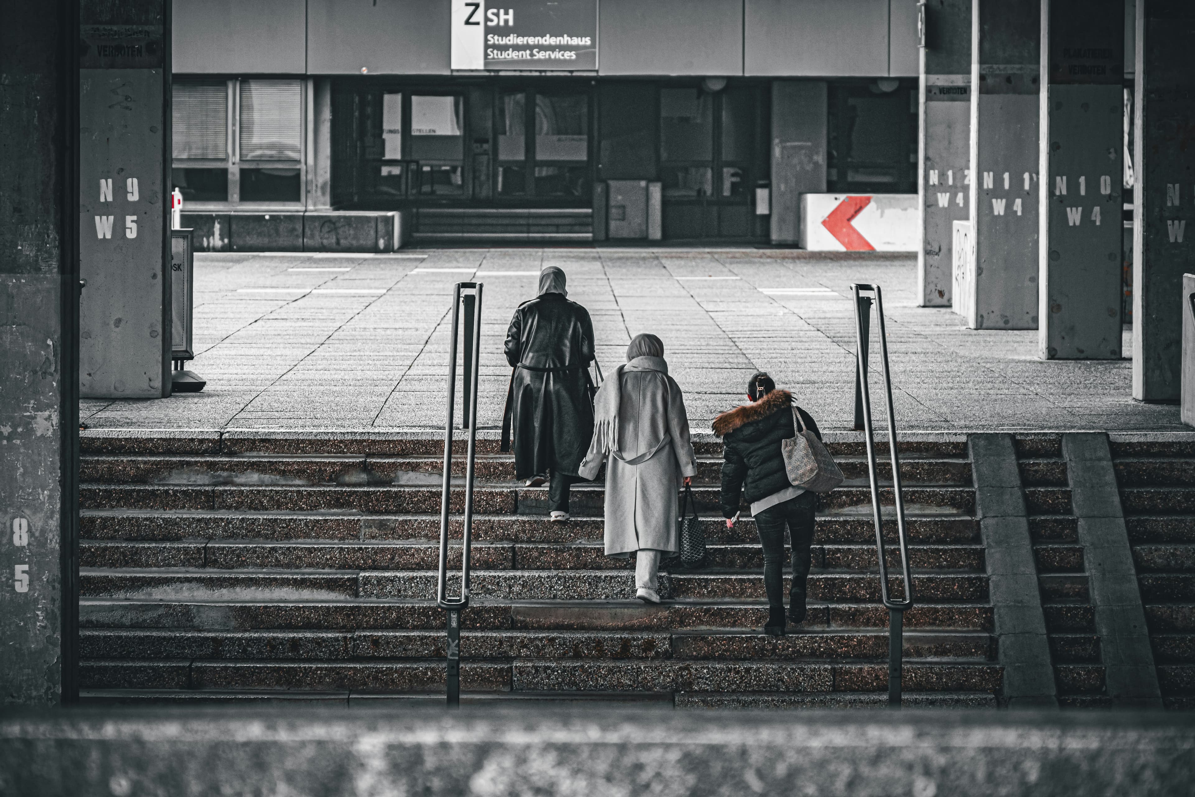 Three people ascend concrete stairs outside building
