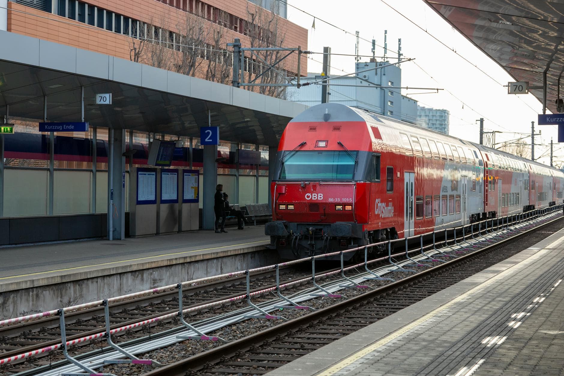 Passenger train at a modern European railway station with industrial architecture and platform signs.