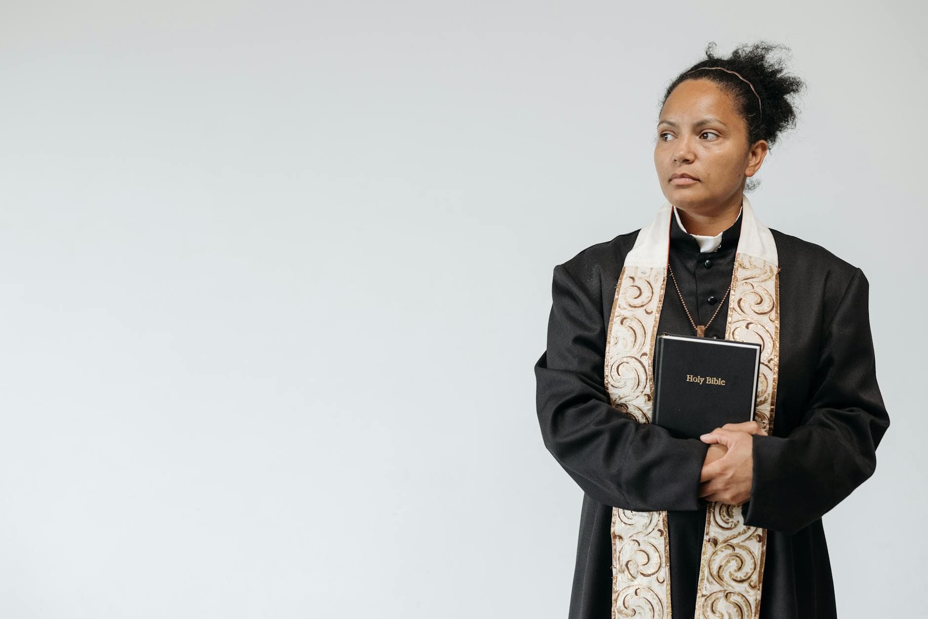 A female priest in religious attire holding a Holy Bible, symbolizing faith and spirituality.