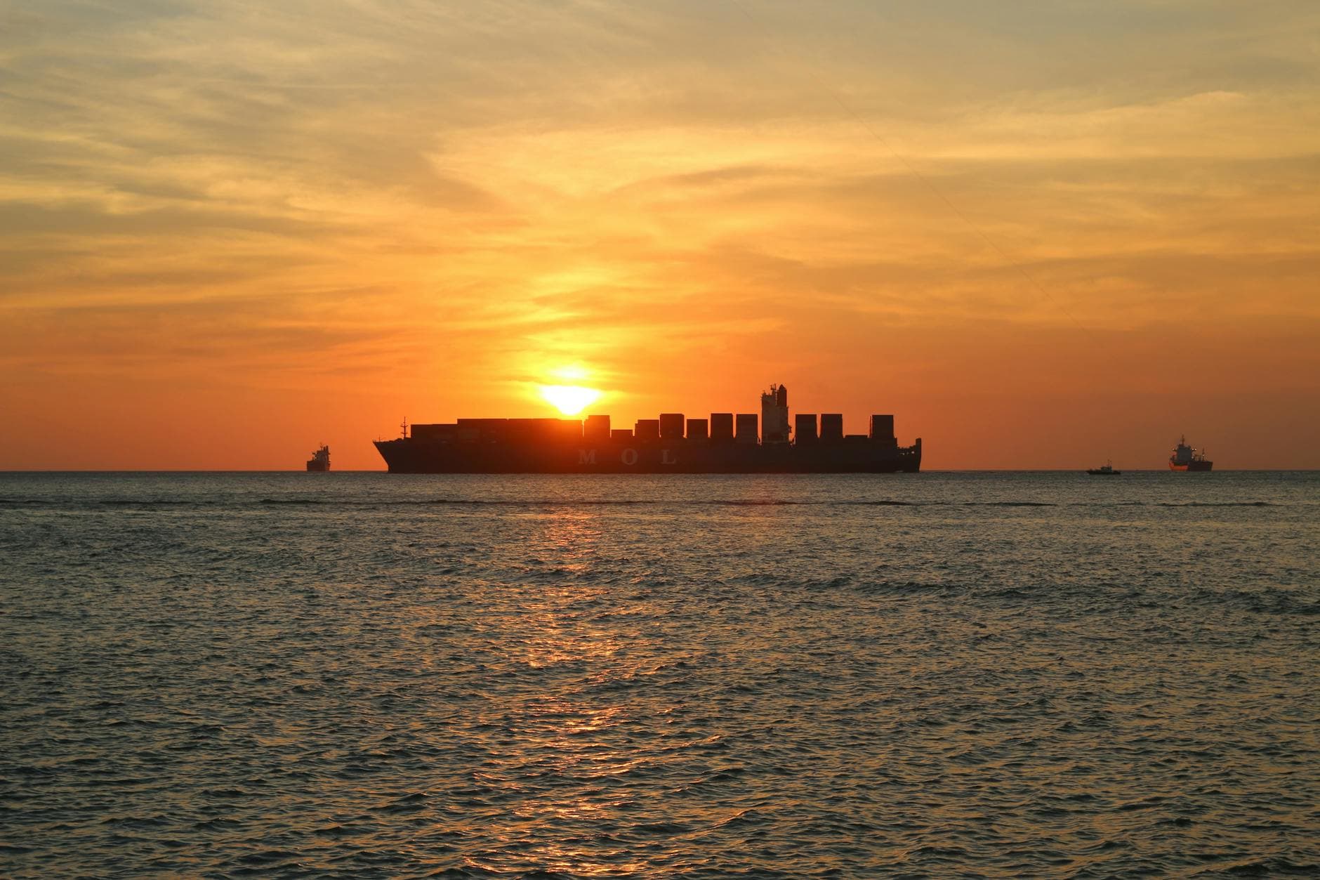Silhouette of a shipping vessel against a vibrant sunset over the ocean, creating a serene seascape.