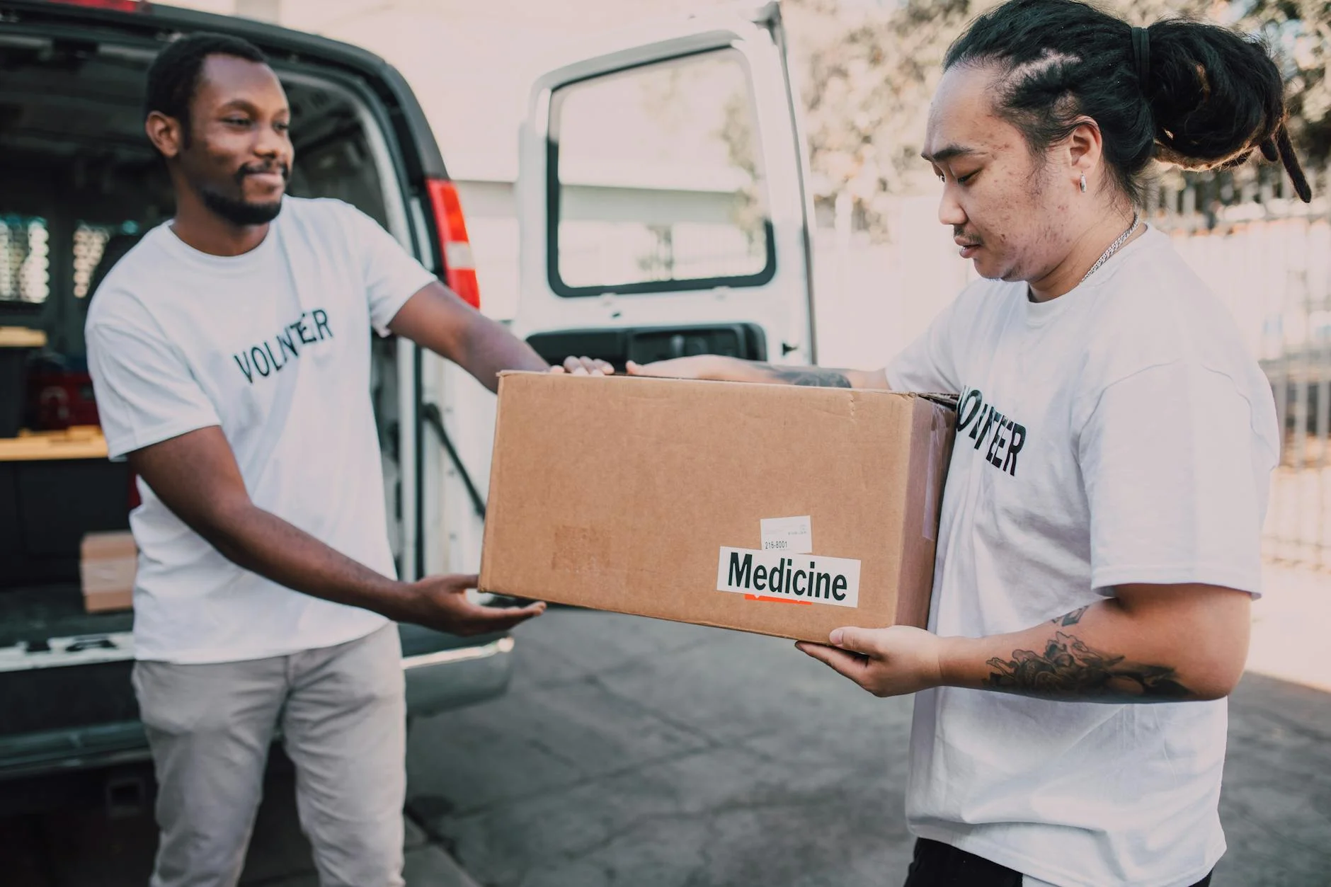 Two volunteers distribute a box of medicine from a van, emphasizing charity and teamwork.