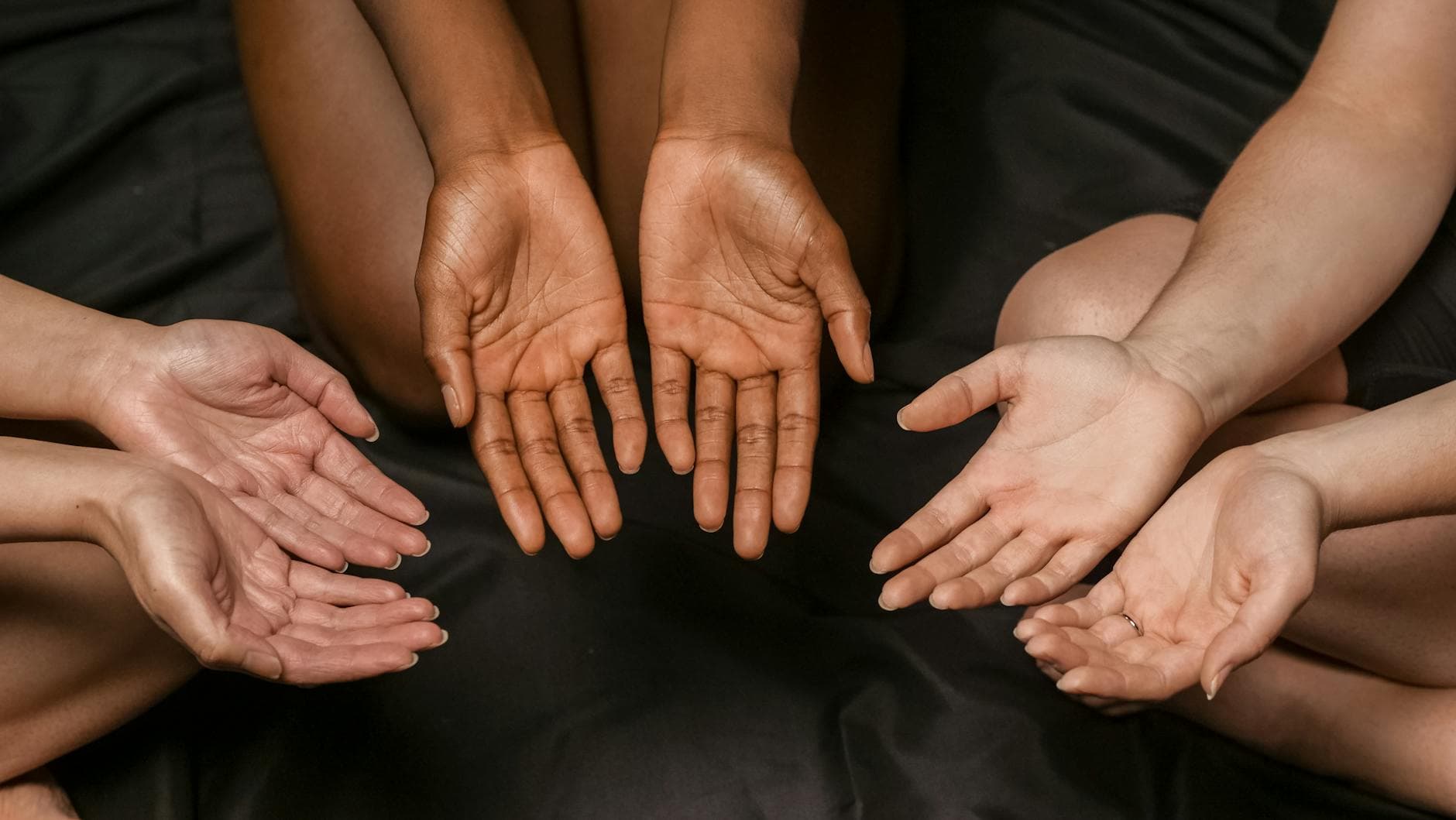 A close-up of diverse hands in a circular formation on a dark surface.