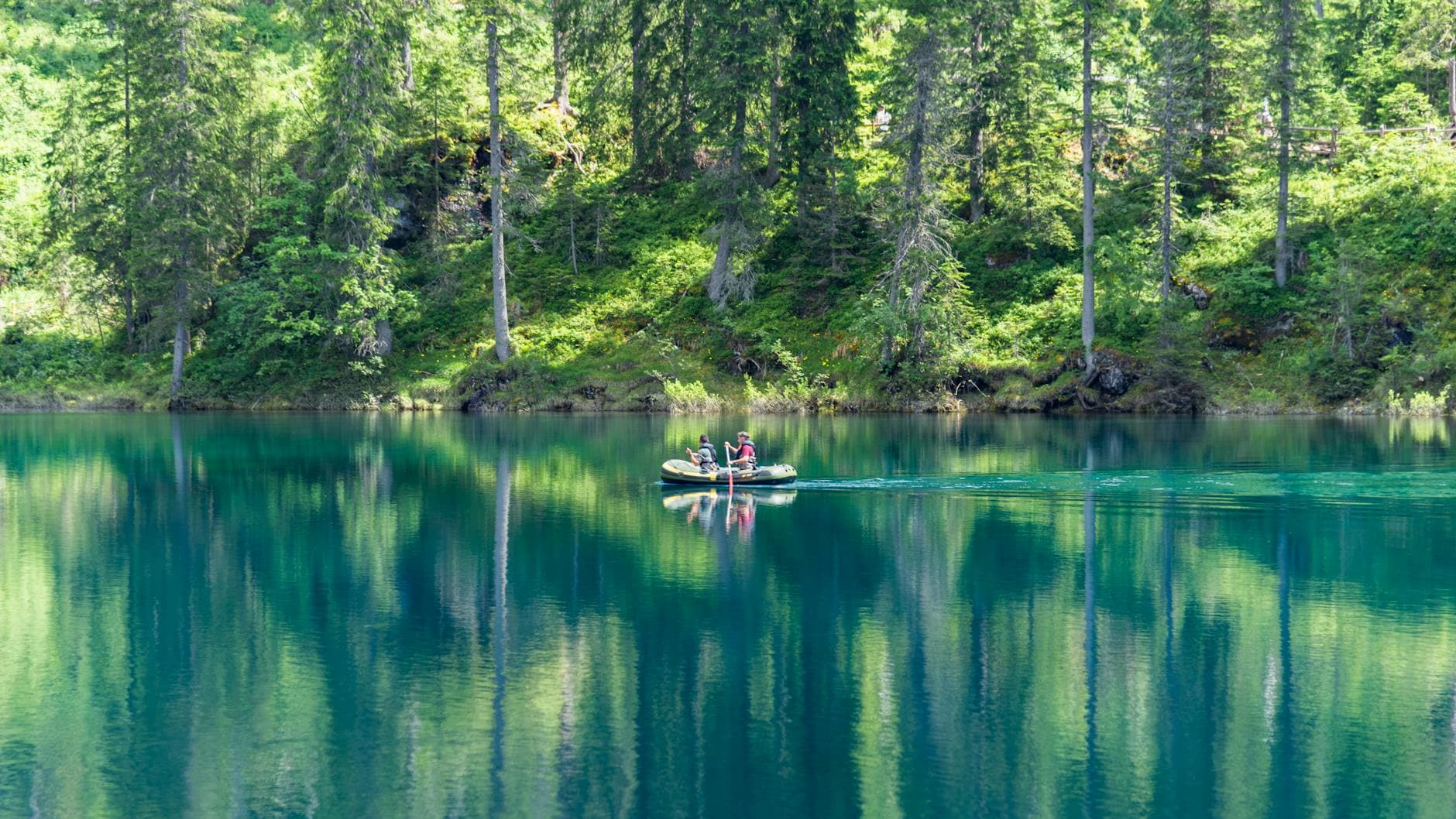 Two people boating on a tranquil lake surrounded by lush forests in Trentino-South Tyrol, Italy.