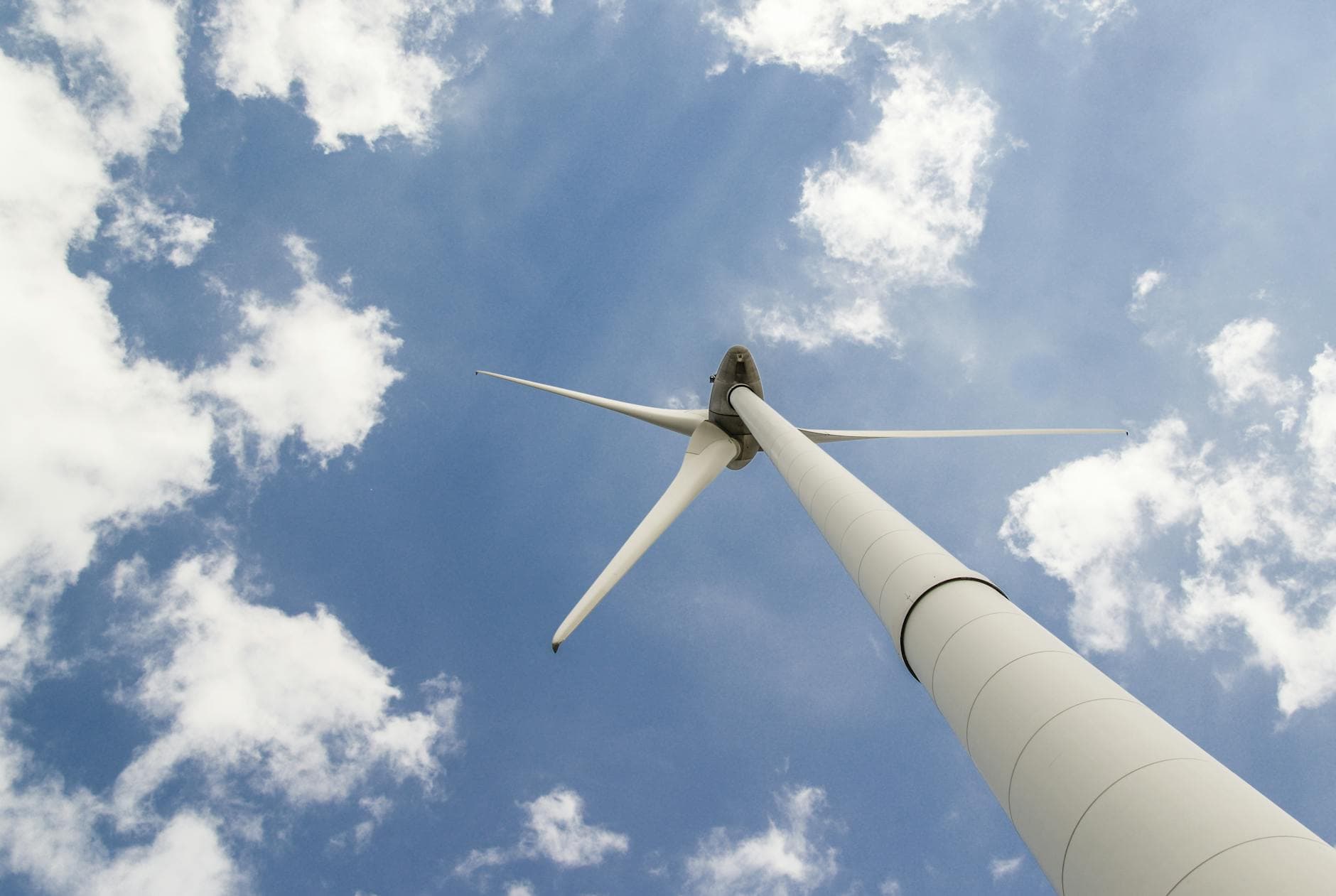 View of a towering wind turbine against a cloudy blue sky, highlighting renewable energy technology.
