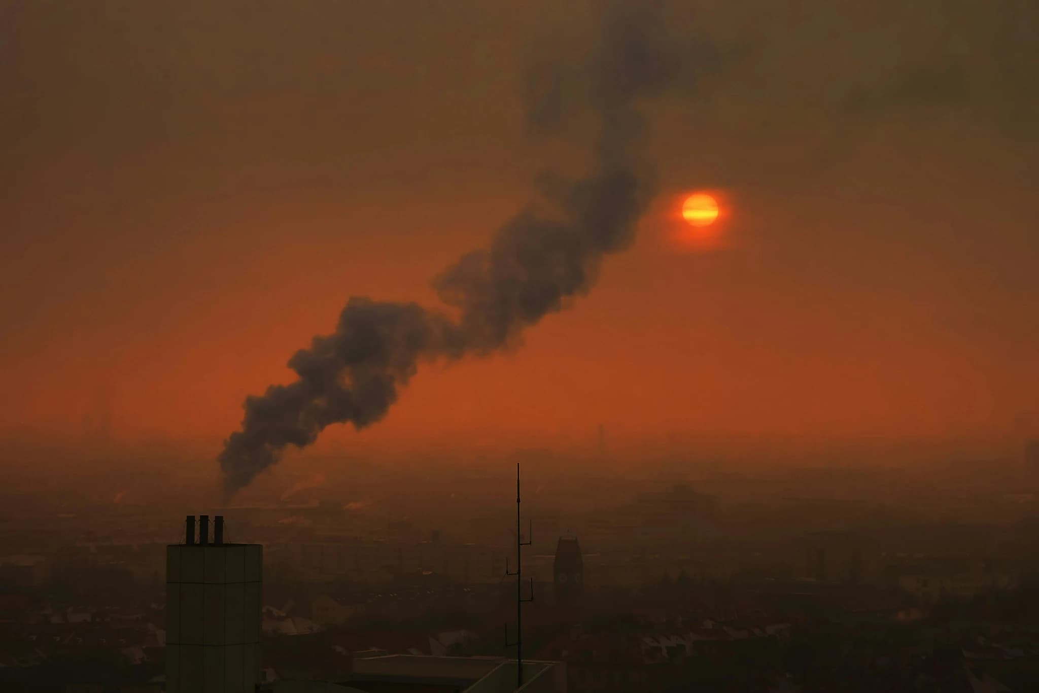 Smoke billows from a chimney against a hazy sunset.