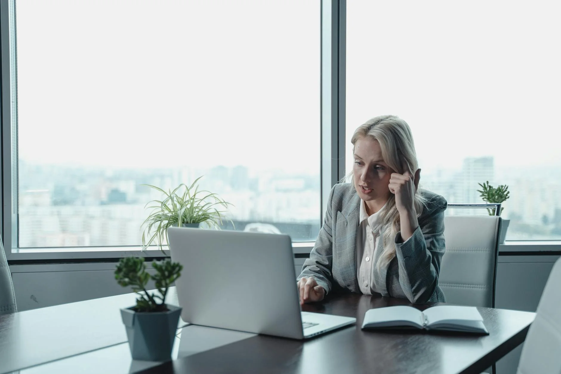 Professional woman engaged in a video meeting at a modern office desk with a laptop.
