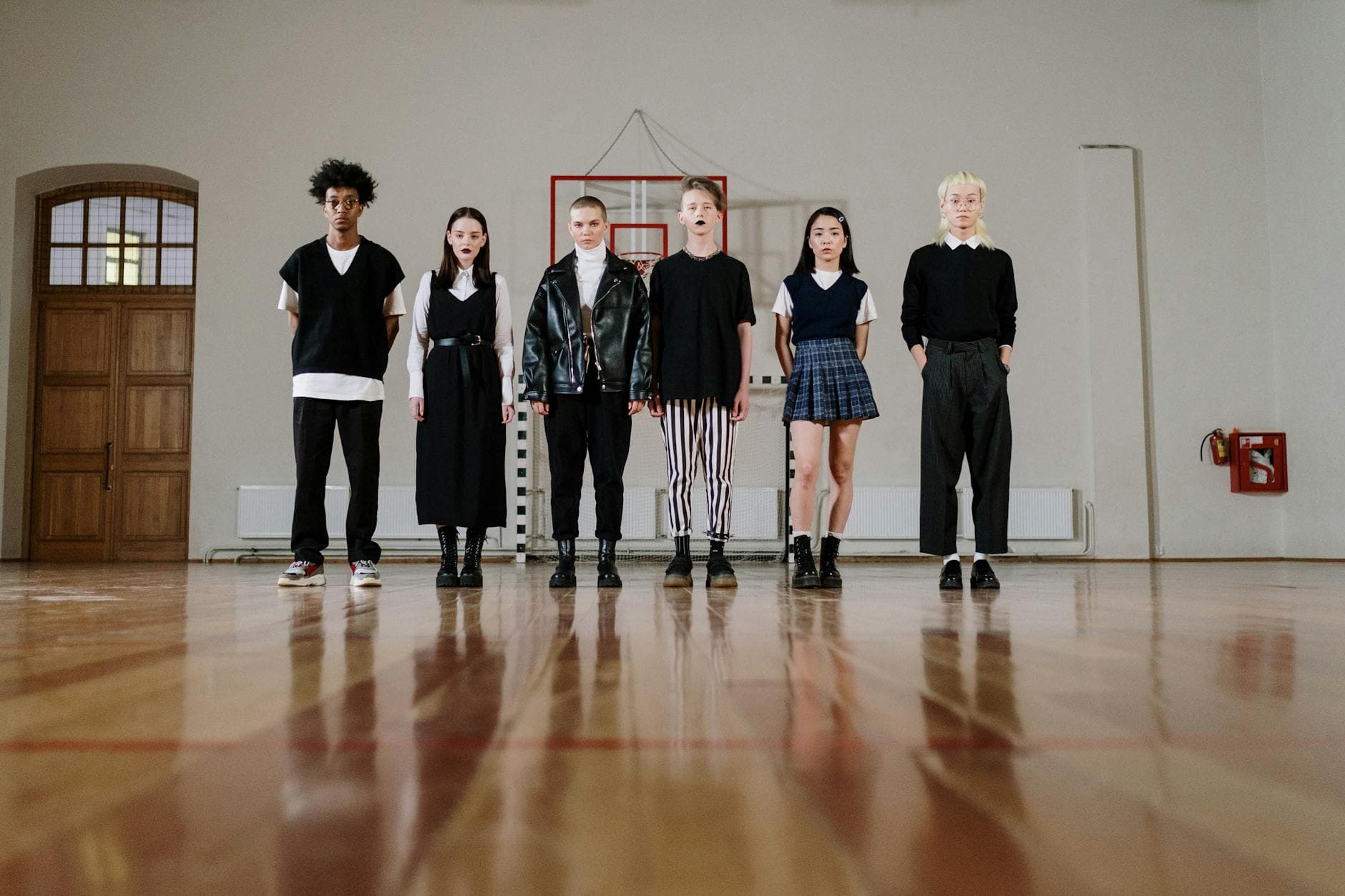 Stylish teenagers standing in a gym, showcasing diverse fashion and camaraderie.
