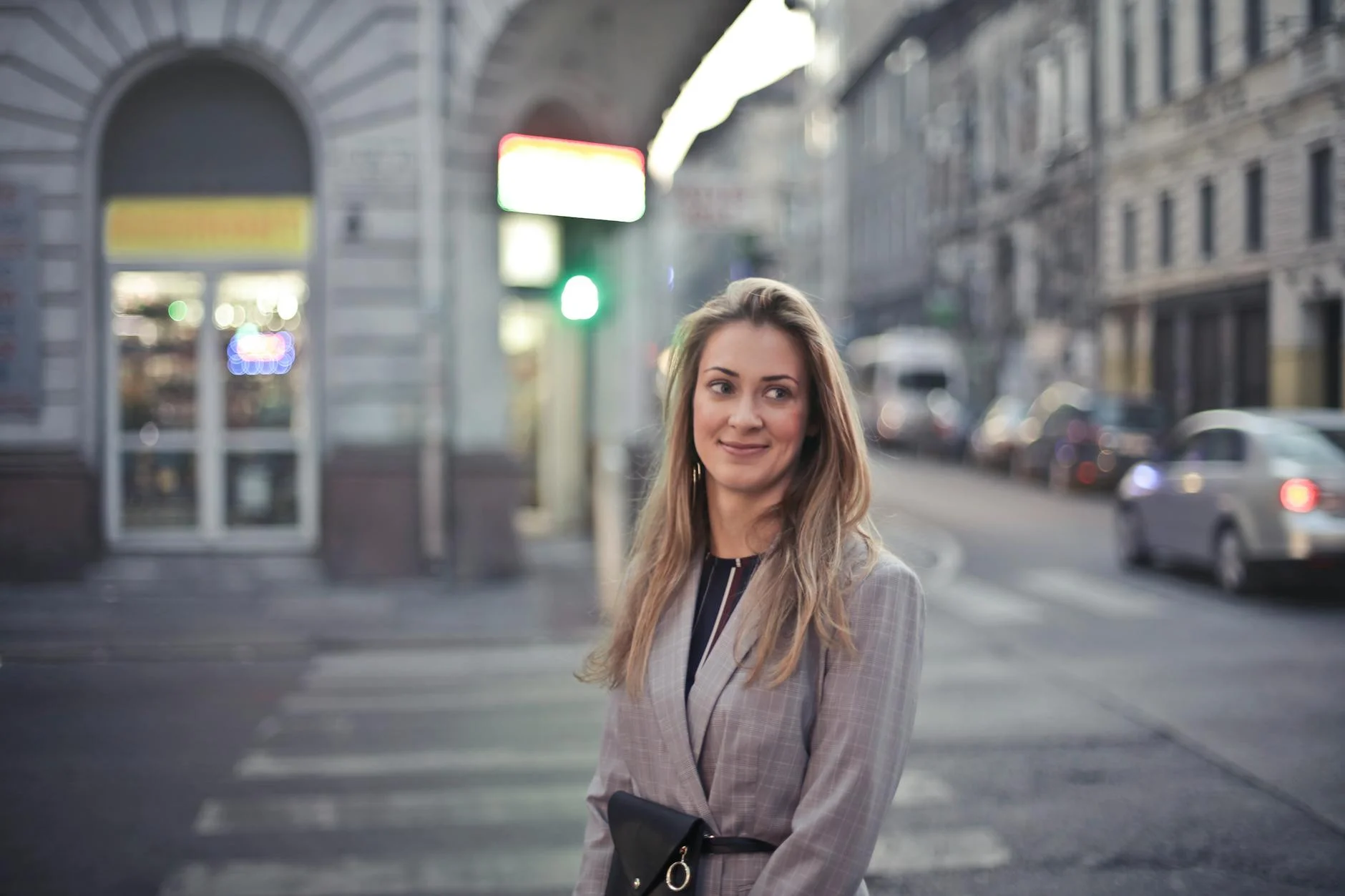 Woman smiling confidently in urban Budapest street scene with vibrant evening lights.