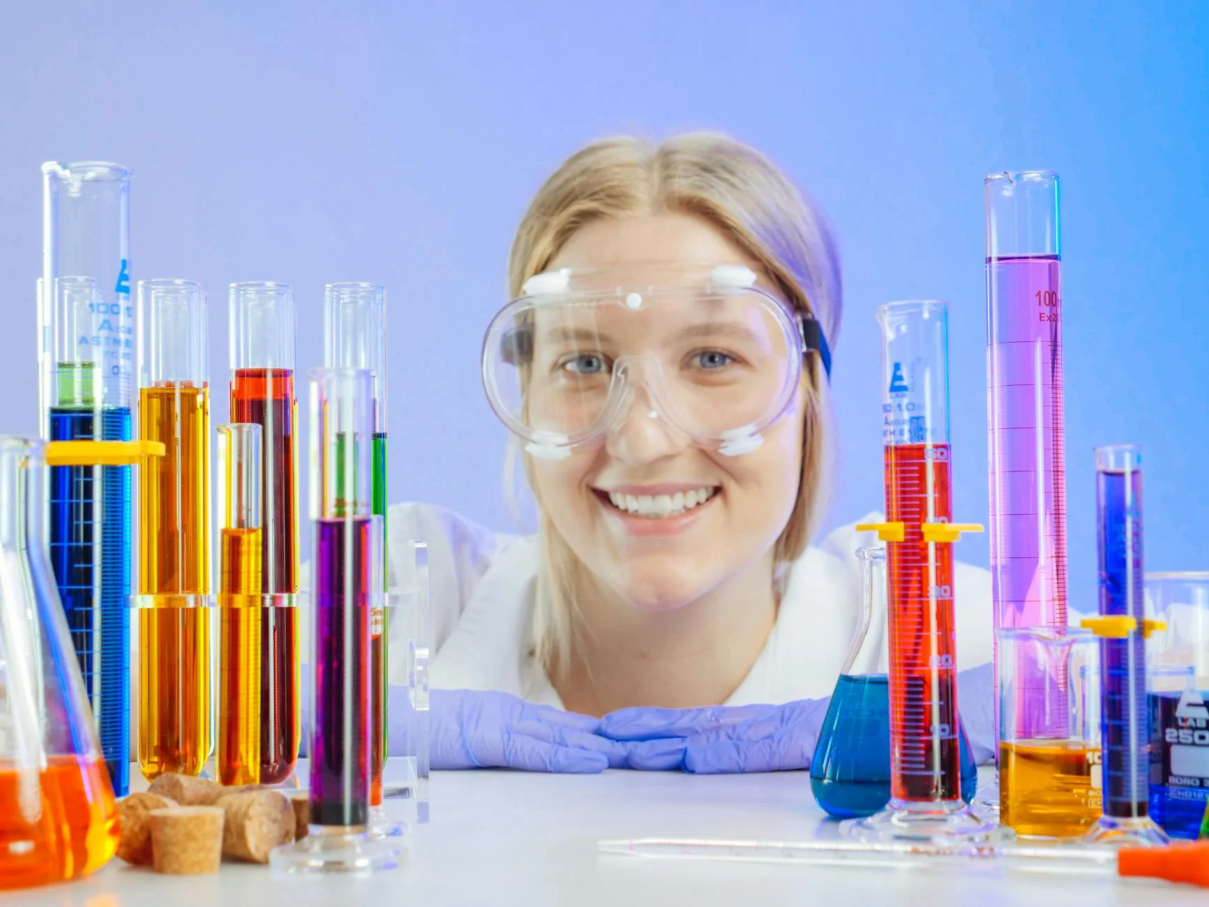 Smiling female scientist with lab glassware filled with colorful liquids.