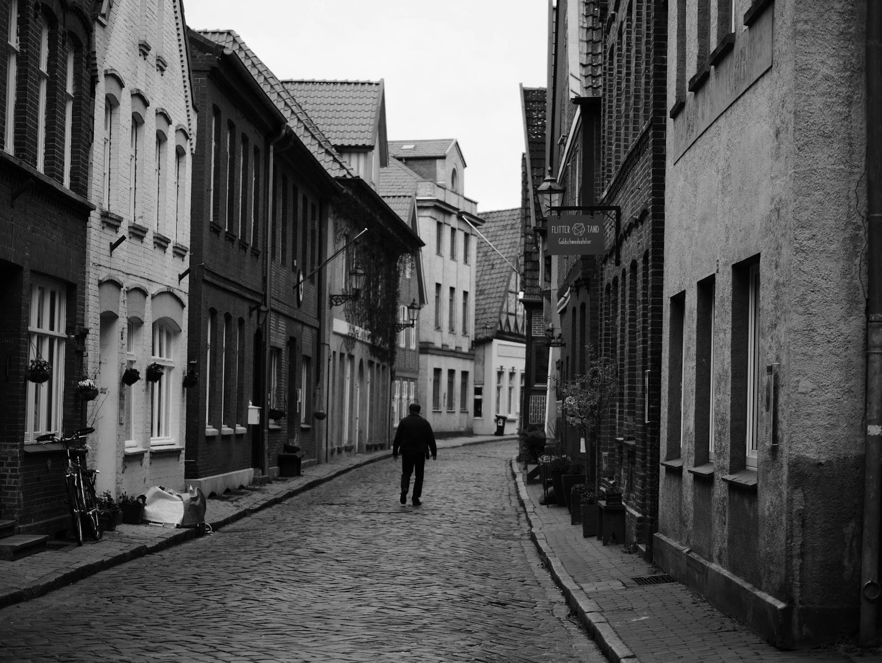 Charming cobblestone street with a person walking, captured in monochrome.
