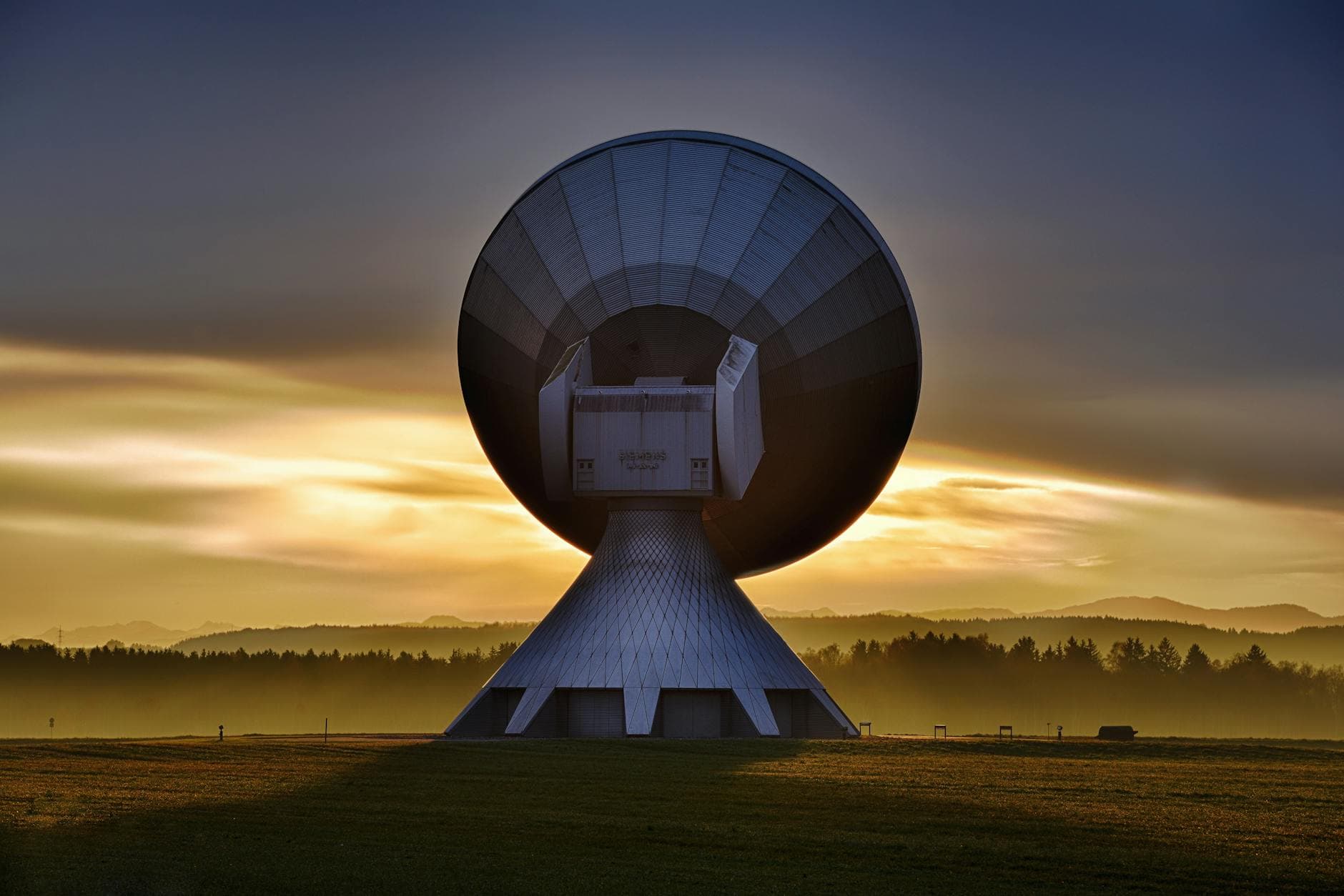 Large satellite dish silhouette against a colorful sunset, showcasing broadcasting technology.