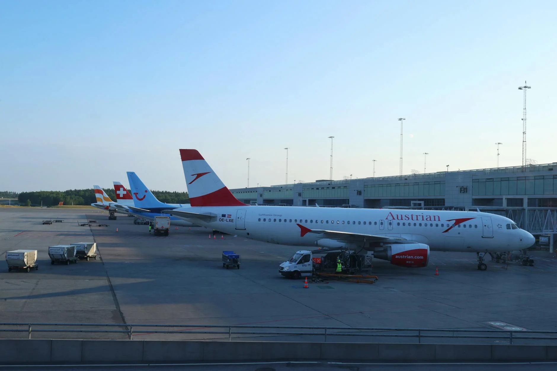 Multiple commercial airplanes stationed at Oslo Airport terminal during the day.