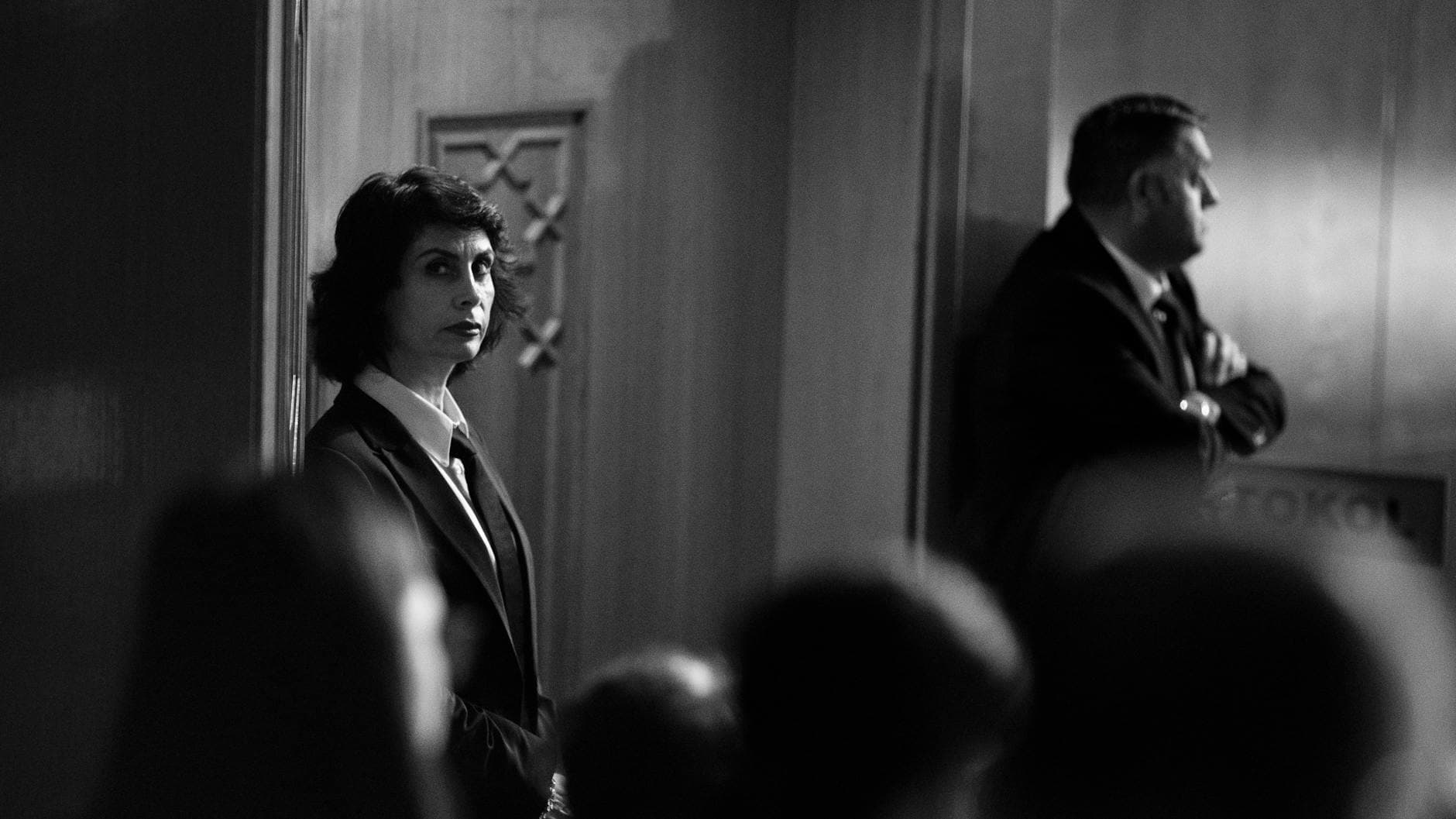 A black and white image of security personnel in suits overseeing a formal event.