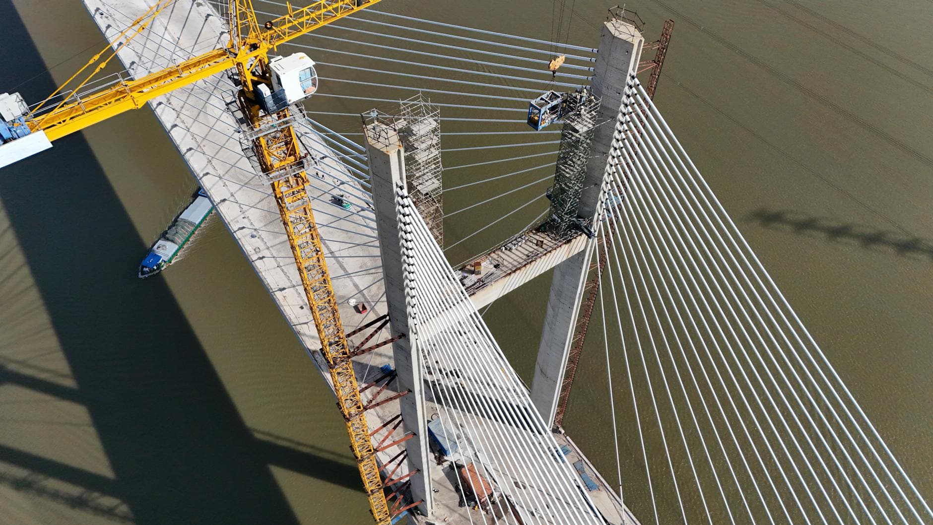 Aerial glance at a cable-stayed bridge under construction, showcasing yellow crane work over a river.