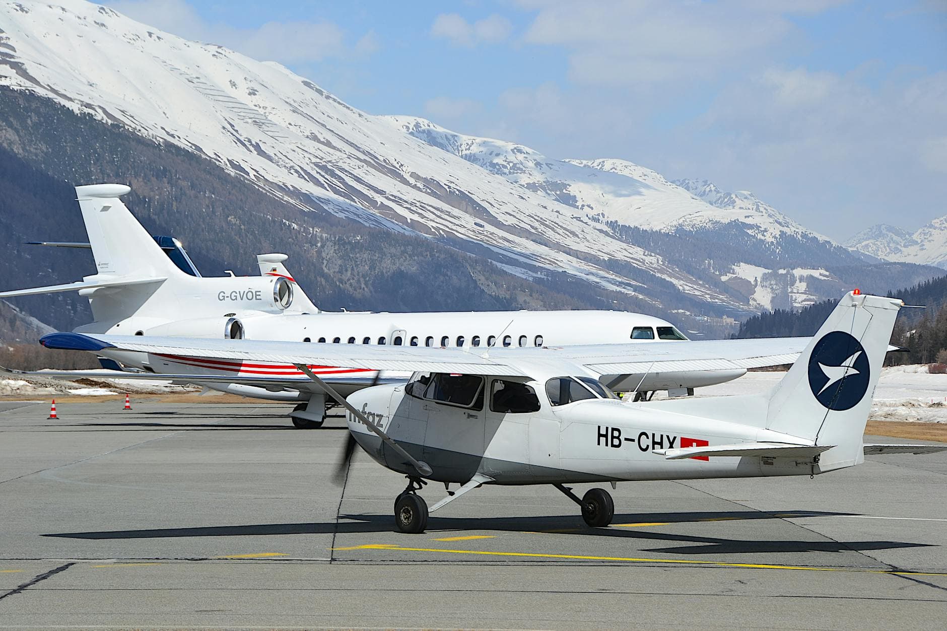 Aircraft parked on a snowy runway in Samedan, Switzerland with mountainous backdrop.