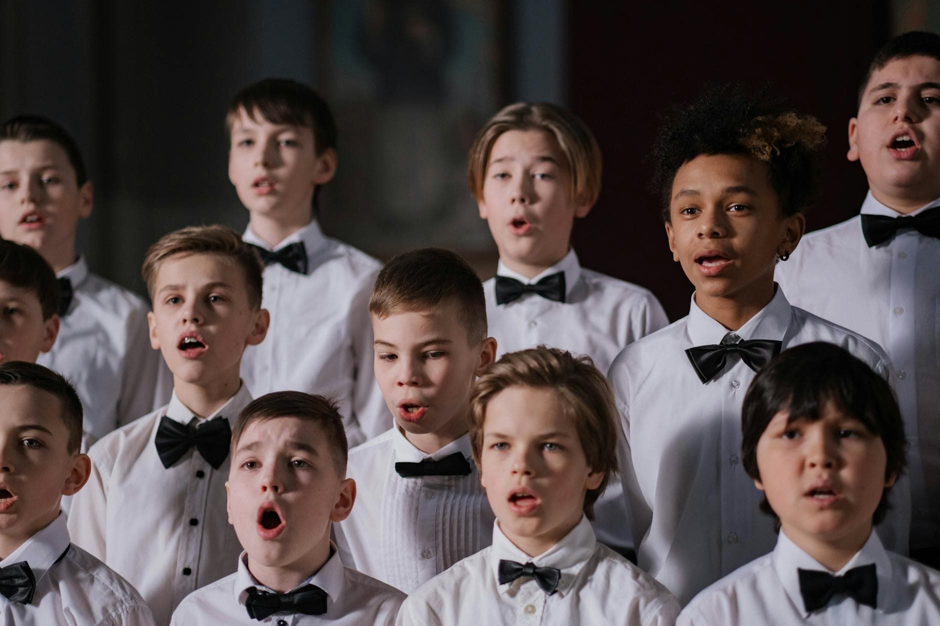 Group of boys performing in a choir, dressed in white shirts and black bowties.