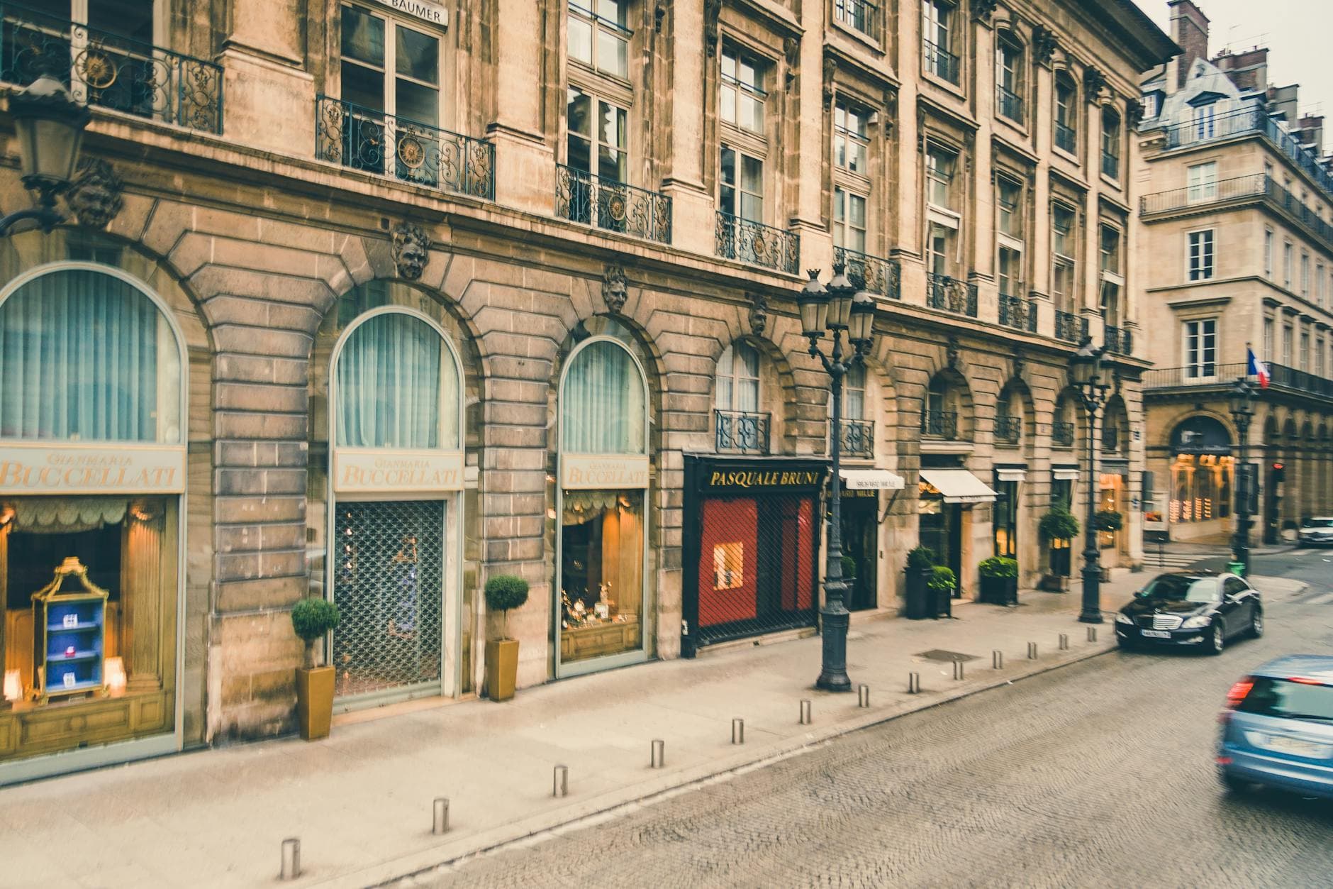Elegant Parisian street with classic architecture, cars, and boutique storefronts.