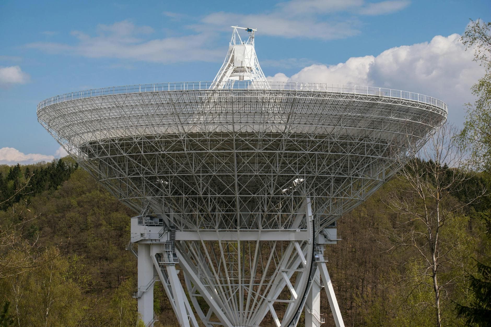 A large radio telescope set against a backdrop of trees and clouds, capturing celestial signals.