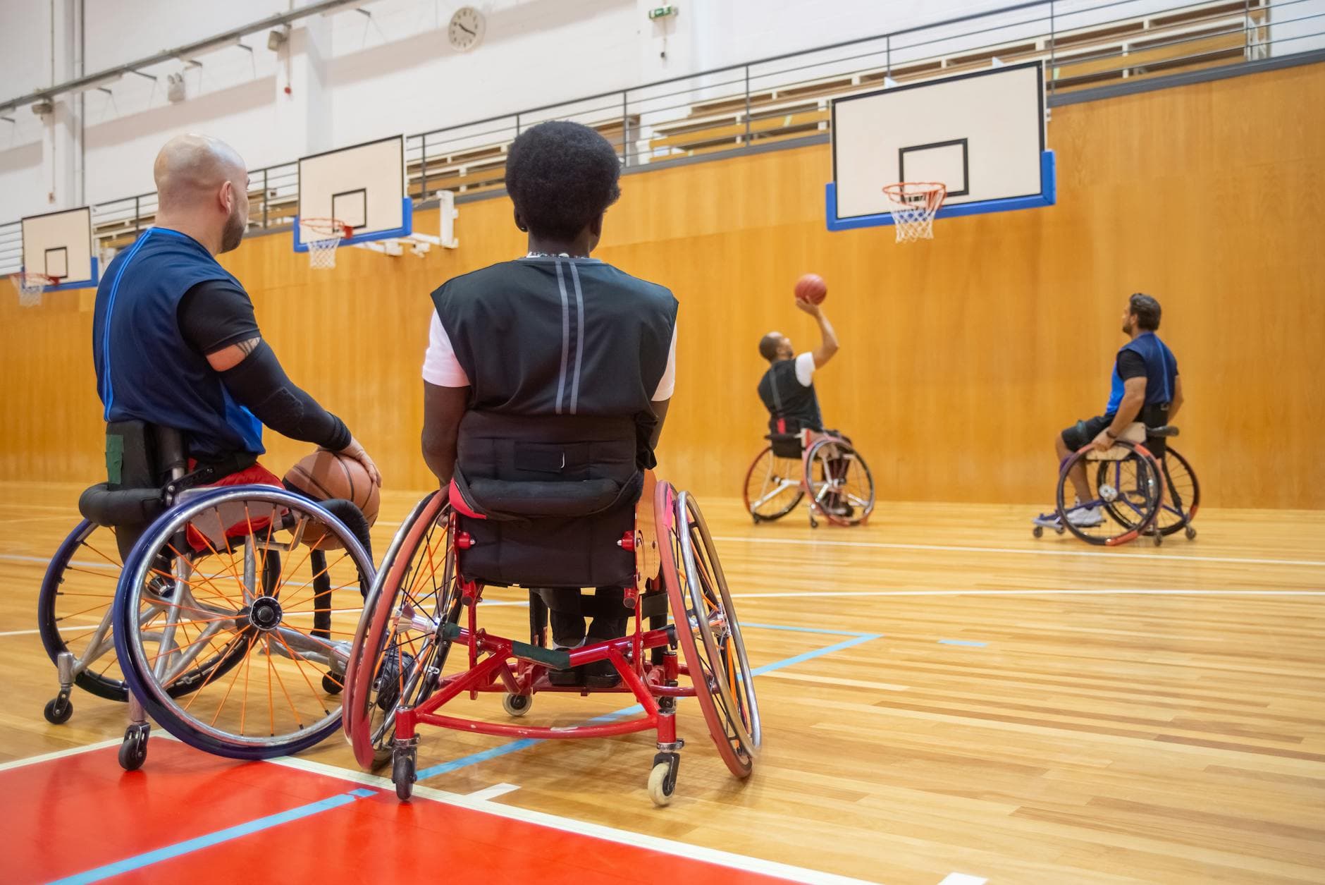 Athletes playing wheelchair basketball during a training session in an indoor sports hall.