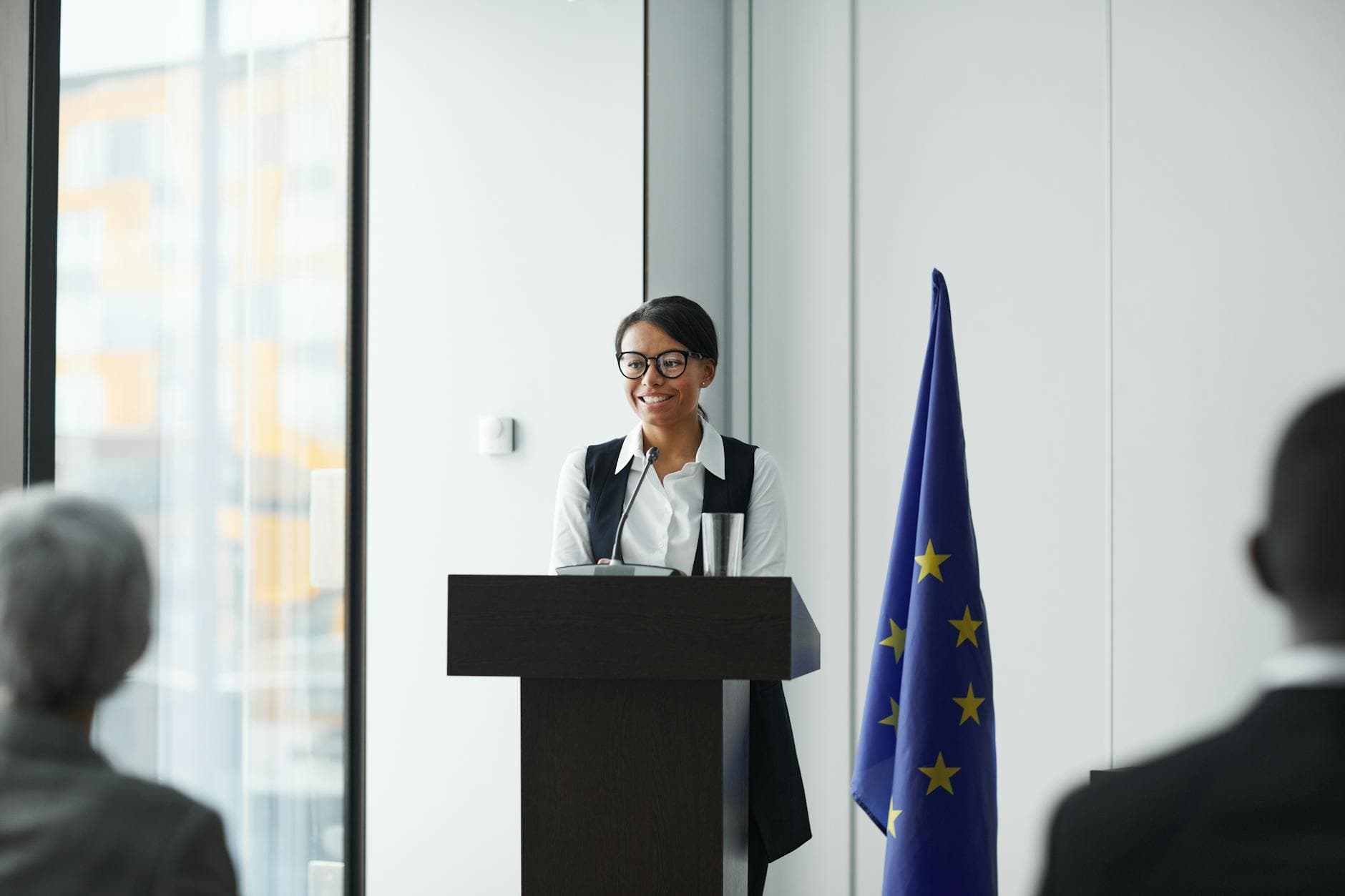A woman giving a speech at a podium with an EU flag in a conference setting.